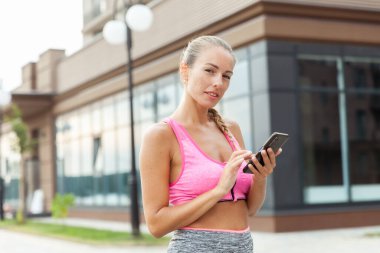 Spor giyim sektöründe formda bir kadın açık havada akıllı telefon kullanıyor.