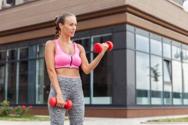 Aktif yaşam tarzı konsepti. Spor giyim bölümünde formda bir kadın, elinde dambıllarla kasları çalıştırıyor.