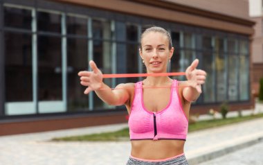Formda bir kadın kol kaslarını dışarıda spor lastiği bantlarıyla çalıştırıyor.
