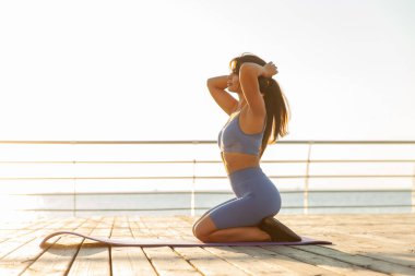 Young fit woman sitting on a yoga mat on the beach and getting ready for a workout