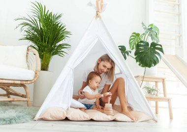 Anne ve kızı, modern minimalist aydınlatma odasında ev bitkileriyle çadır kurarken gelişmekte olan bir piramitle oynuyorlar.