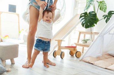 Annem küçük kızına modern bir oyun odasında yürümeyi öğretiyor. İlk adımlar