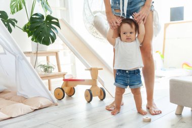 Annem küçük kızına modern bir oyun odasında yürümeyi öğretiyor. İlk adımlar