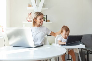 Mom and her little daughter use laptops and sit at the tables at home. Maternity, work and maternity