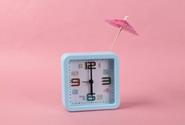 Pembe arka planda kokteyl şemsiyeli çalar saat. Asgari natürmort, düzen