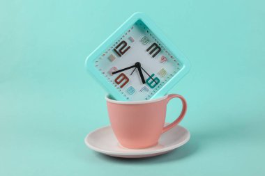 Mavi zemin üzerinde alarm saati olan seramik bardak