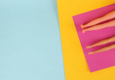 Plaj tatili kavramı. Oyuncak bebeklerin bacakları bir paspasın üzerinde uzanıyor ve sarı mavi arka planda güneşleniyor. En küçük yerleşim