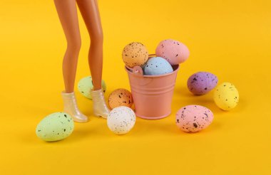 Sarı arka planda renkli paskalya yumurtalarının olduğu oyuncak bebek ayakları. Paskalya Minimum Konsepti