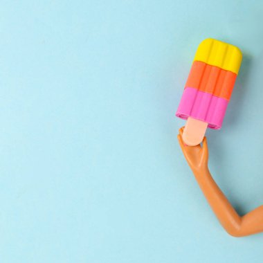 Bebeğin elinde, mavi arka plandaki bir çubuğun üzerinde donmuş meyve suyu var.