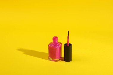 Sarı arka planda pembe tırnak cilası şişesi uzun gölgeli.