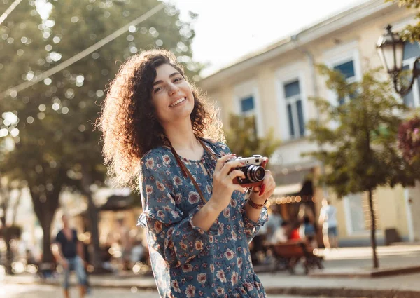 Şehirde geçmişe dönük kamerası olan kıvırcık kadın fotoğrafçı.