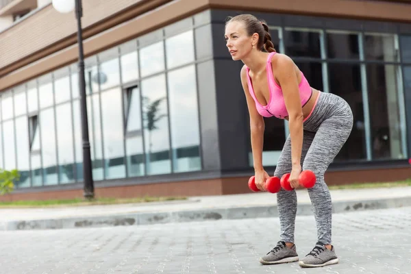 Aktif yaşam tarzı konsepti. Spor giyim bölümünde formda bir kadın, elinde dambıllarla kasları çalıştırıyor.