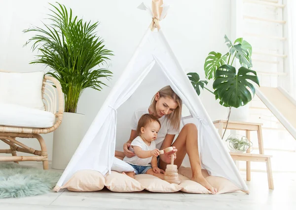 Anne ve kızı, modern minimalist aydınlatma odasında ev bitkileriyle çadır kurarken gelişmekte olan bir piramitle oynuyorlar.