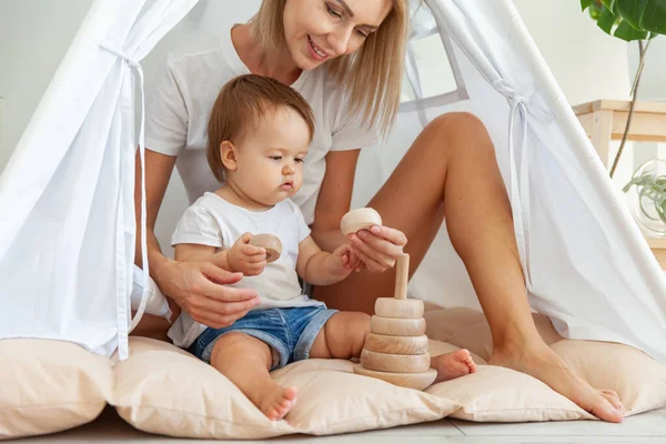 Mamoly 'li küçük bir kız, evde bir çadırda otururken, motor becerilerini geliştirmek ve düşünmek için tahta, katlanabilir bir piramitle oynar.