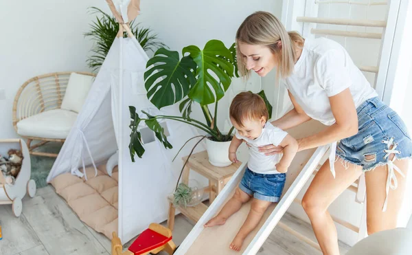 Genç bir anne küçük kızıyla oyun odasında oynar. Kız kaydırağından aşağı yuvarlanıyor