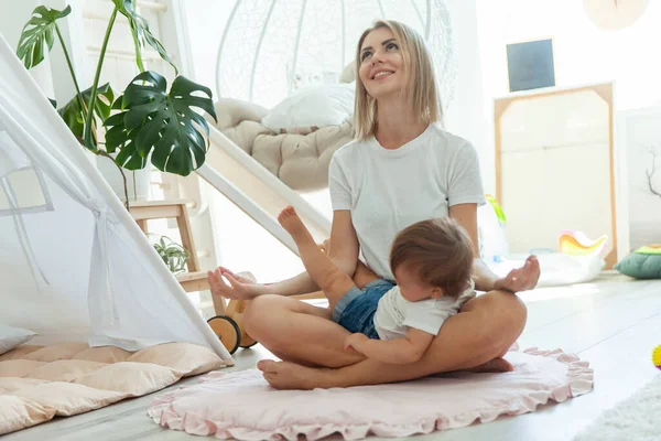 Genç anne küçük kızıyla evde nilüfer çiçeği pozisyonunda meditasyon yaparak vakit geçiriyor. Rahatla ve stres kavramının üstesinden gel.