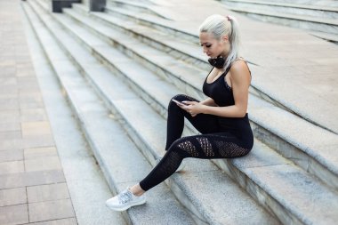 Spor salonundaki kadın merdivenlerde otururken akıllı telefon kullanıyor.