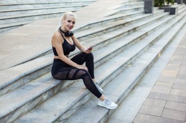 Spor salonundaki kadın merdivenlerde otururken akıllı telefon kullanıyor.