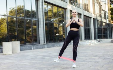 Spor salonundaki kadın spor yapıyor. Açık havada lastik bantlarla.