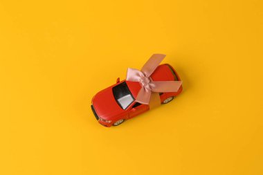 Oyuncak araba modeli sarı arka planda fiyonklu hediye kurdelesini geri sardı. Araba hediye, sürpriz.