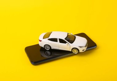 Sarı arka planda akıllı telefonu olan oyuncak araba modeli.