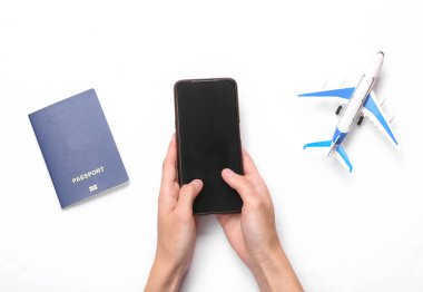Seyahat konsepti. Beyaz arka planda pasaport ve oyuncak uçakla akıllı telefon kullanılıyor.