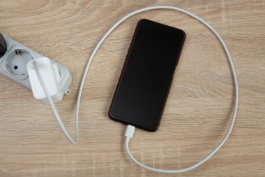 Akıllı telefon ve şarj aleti ahşap masada. Üst görünüm