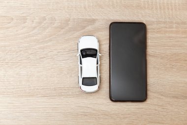 Ahşap masada akıllı telefonu olan oyuncak araba modeli.