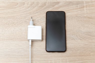 Tahta masada şarj aleti olan akıllı telefon.