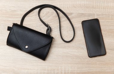 Ahşap bir masanın üzerinde akıllı telefon bulunan deri bir çanta. Üst görünüm