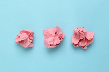 Açık mavi arka planda buruşmuş pembe kağıtlar. Asgari konsept