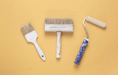 Sarı arka planda boya fırçaları ve silindirler. Onarım sembolü