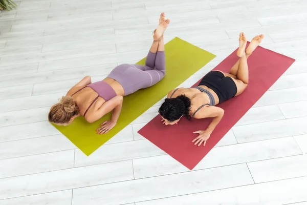 Two fit women push up from the floor together indoors