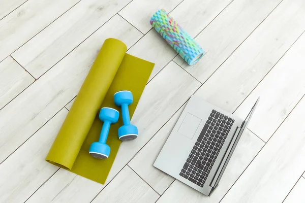 Laptop with dumbbells, rug and massage roller on the floor. Online fitness class, or sports tutorial