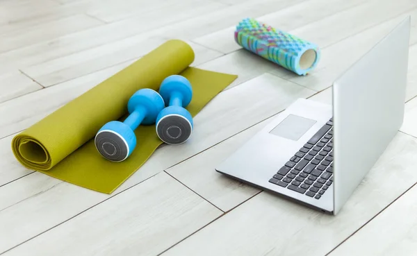 Laptop with dumbbells, rug and massage roller on the floor. Online fitness class, or sports tutorial