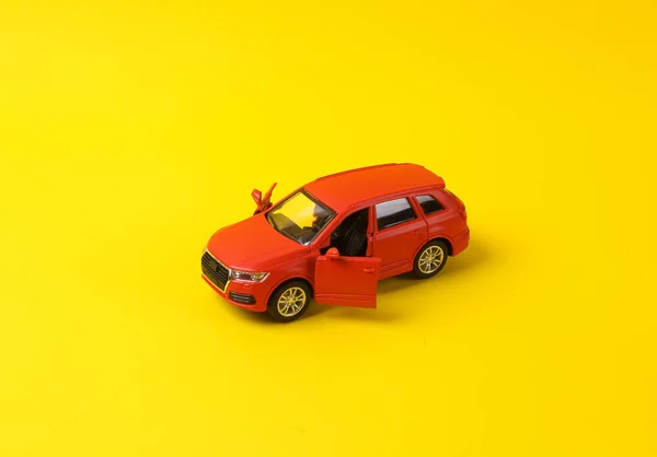 Mini model of red toy car with open doors on yellow background