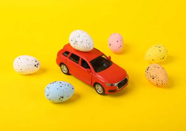 Model of a toy car with Easter eggs on a yellow background. Minimal easter still life