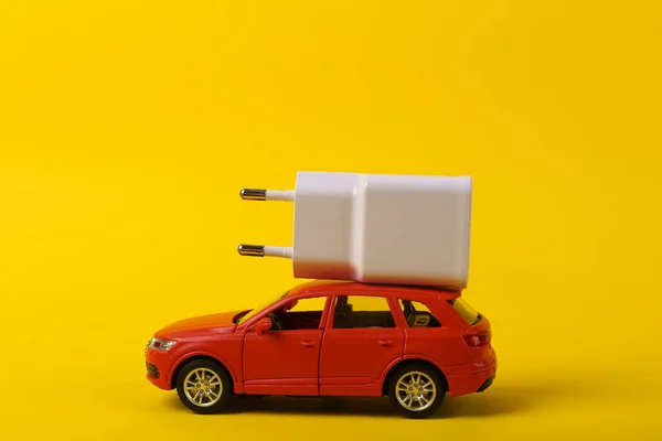 Sarı Arka Planda Şarj Aleti Olan Oyuncak Bir Araba Elektrikli — Stok fotoğraf