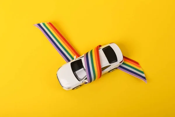 Toy model auto wrapped in rainbow lgbt tape on yellow background