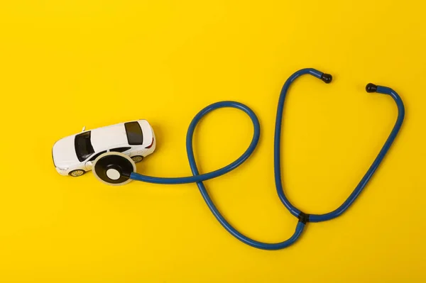 Toy car model with a stethoscope on a yellow background. Car breakdown diagnostics concept. Service center, auto workshop.
