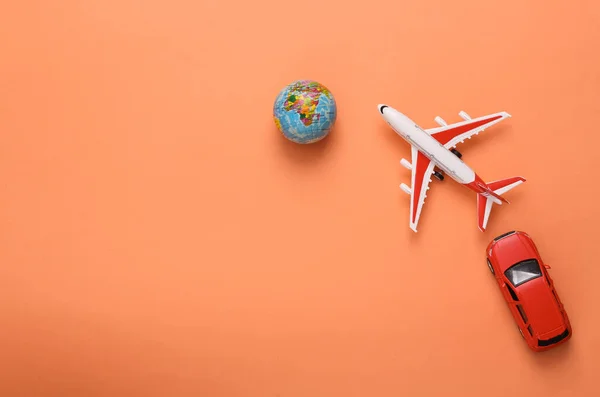 Travel concept. Toy model of car and airplane, globe on coral-colored background. Top view. Copy space