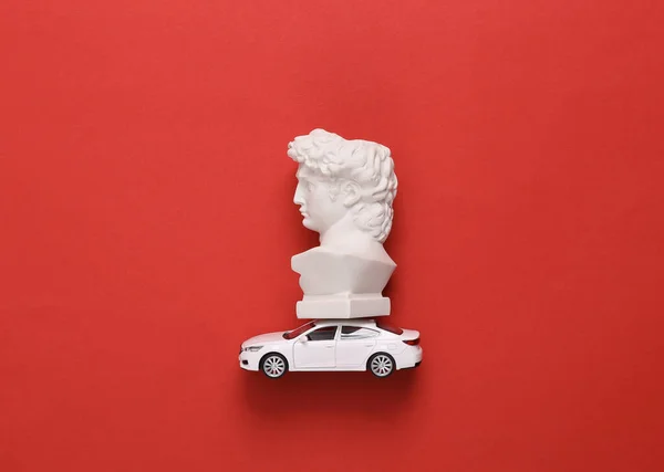 Minimalistic still life. Bust of David on a model car, red background
