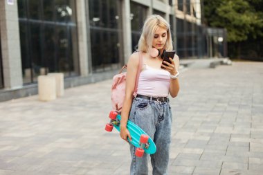 Şehirde akıllı telefon kullanan kaykaylı havalı bir genç kız.