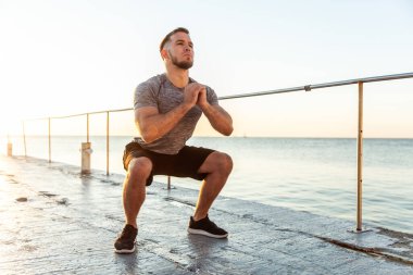 Athletic man practicing squats in the early morning on the beach
