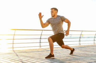 Genç atletik adam sabahın erken saatlerinde sahilde egzersiz yapmadan önce ısınma egzersizi yapıyor. Sağlıklı yaşam tarzı