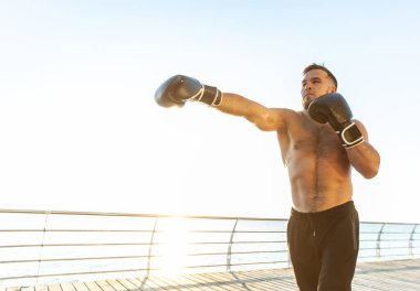Boks eldivenli atletik adam sabahın erken saatlerinde plajda boks yapıyor.