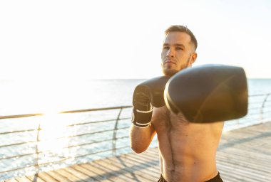 Boks eldivenli atletik adam sabahın erken saatlerinde plajda boks yapıyor.