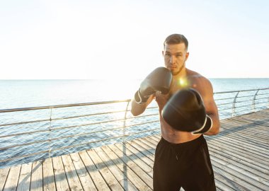 Boks eldivenli atletik adam sabahın erken saatlerinde plajda boks yapıyor.