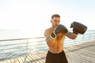 Boks eldivenli atletik adam sabahın erken saatlerinde plajda boks yapıyor.