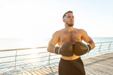 Boks eldivenli atletik adam sabahın erken saatlerinde plajda boks yapıyor.